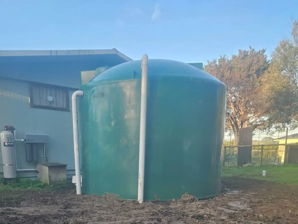 Green poly water tank installed beside a house in Northland, with downpipes connected and a water filtration unit on the wall