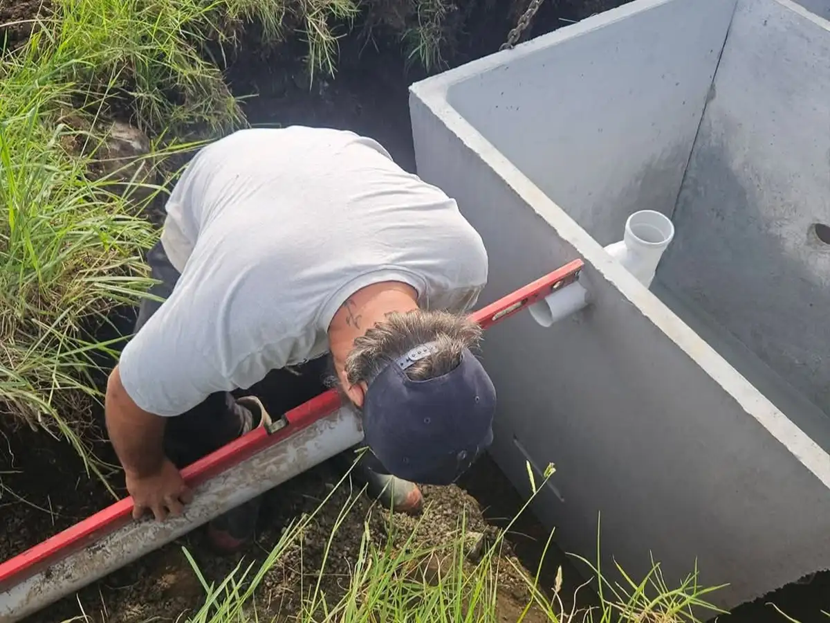 Drainlayer checking the fall on the inlet pipe of a new concrete septic tank at a Northland bach